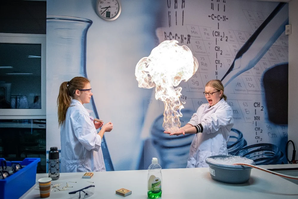 Twee leerlingen reageren op een demonstratie met vuur in het practicumlokaal van het Dr. Nassau College