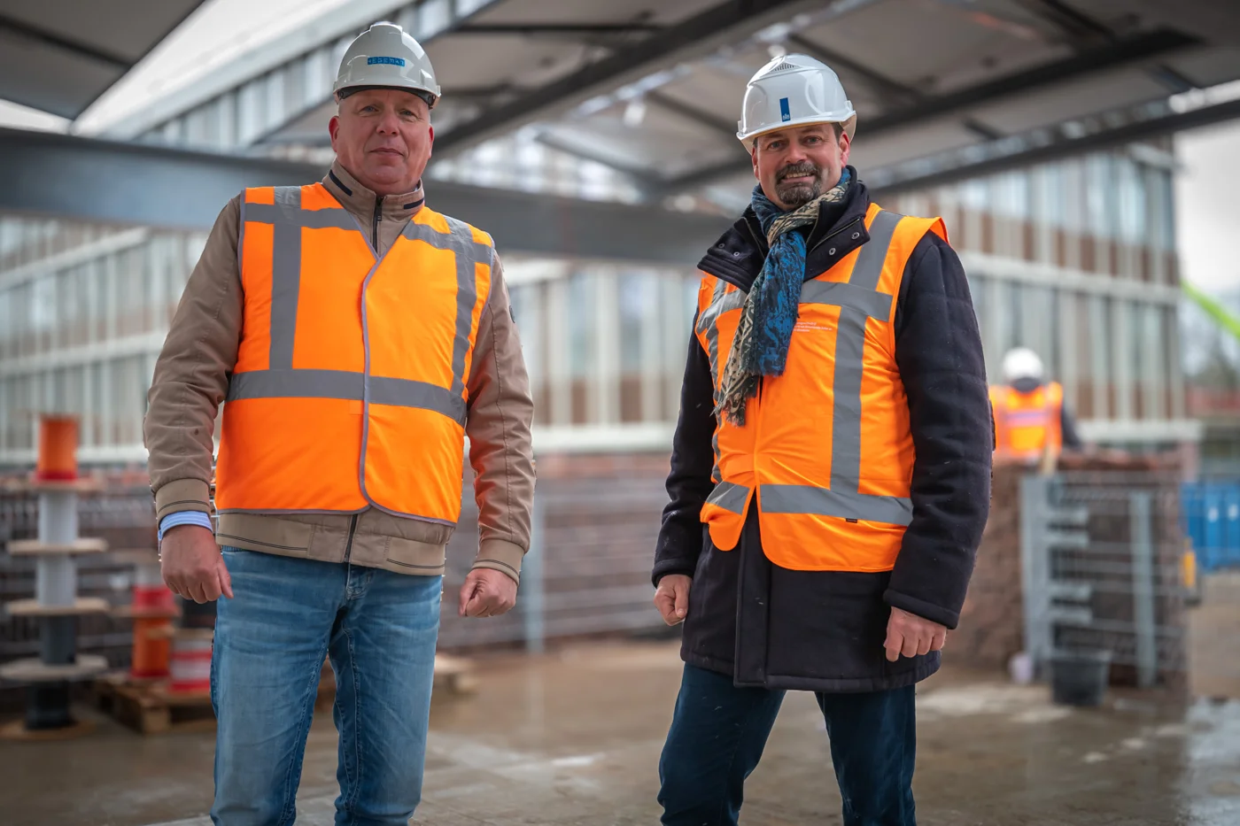 Portret van twee mannen met bouwhelmen en oranje veiligheidsvesten op de bouwplaats